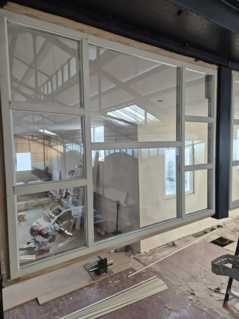 Nieuw geplaatst kozijn met glas in renovatie-atelier met houten balken en gereedschap