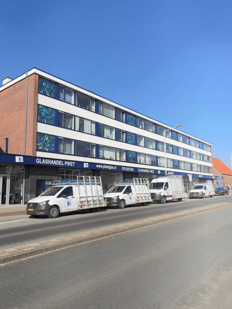 Bedrijfspand Glashandel Piket Den Haag met drie witte servicewagens aan de Westduinweg